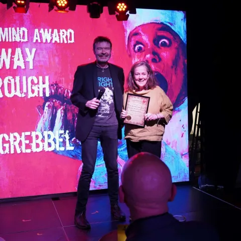 People are seated at small round tables in a dimly lit venue, watching a presentation on stage with a screen displaying "TWISTED50 VOL IV AWARDS.