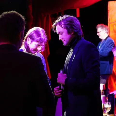 People are seated at small round tables in a dimly lit venue, watching a presentation on stage with a screen displaying "TWISTED50 VOL IV AWARDS.