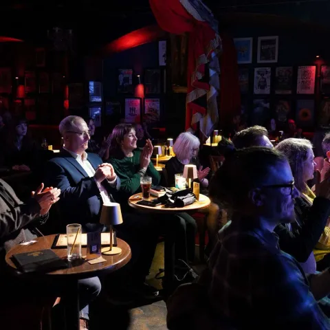People are seated at small round tables in a dimly lit venue, watching a presentation on stage with a screen displaying "TWISTED50 VOL IV AWARDS.