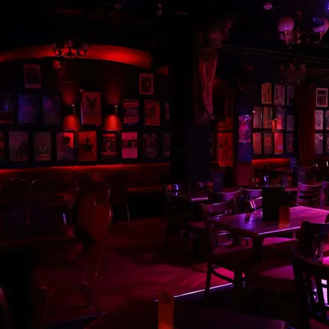 A woman smiles while talking to a man in a dimly lit bar with neon signage in the background.