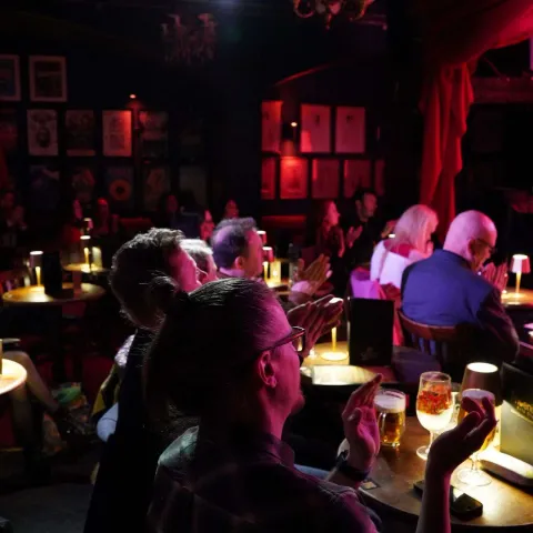 A woman smiles while talking to a man in a dimly lit bar with neon signage in the background.