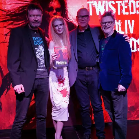 People are seated at small round tables in a dimly lit venue, watching a presentation on stage with a screen displaying "TWISTED50 VOL IV AWARDS.