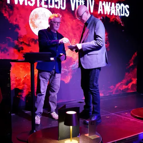 A group of people on stage receive awards, standing in front of a red screen that reads "TWISTED50 VOL 3 WINNERS" under stage lighting.