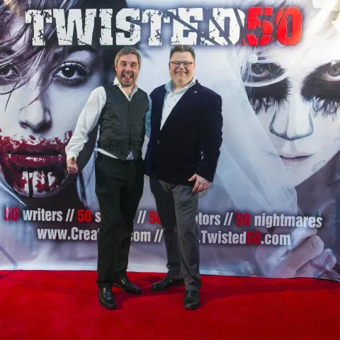 Two men standing in front of a poster for twisted 50.