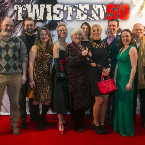 A man and woman posing in front of a poster for twisted 50.