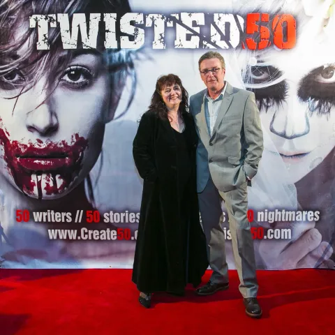A man and woman posing in front of a poster for twisted 50.