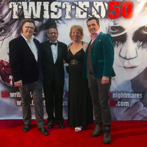 A man and woman posing in front of a poster for twisted 50.