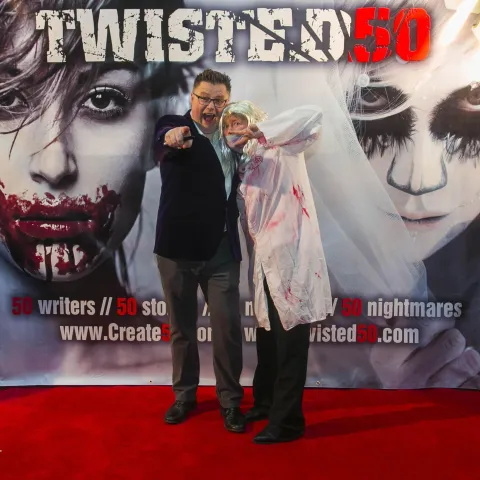 Two men standing in front of a poster for twisted 50.