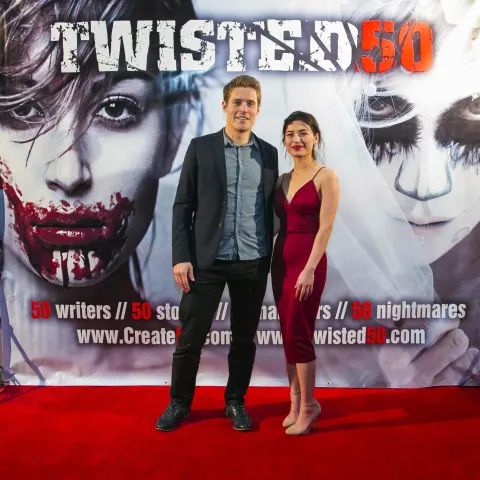 A man and woman posing in front of a poster for twisted 50.